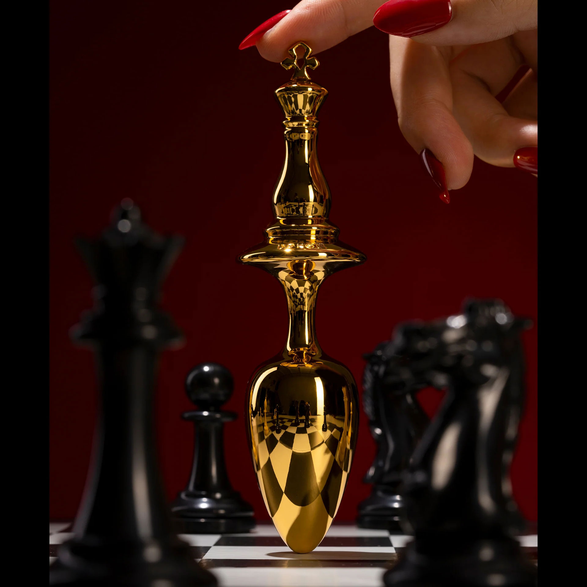 »The Chess« König Plug - Bild 2 Ein Analplug mit einer Königskrone zwischen Schachfiguren auf einem Schachbrett