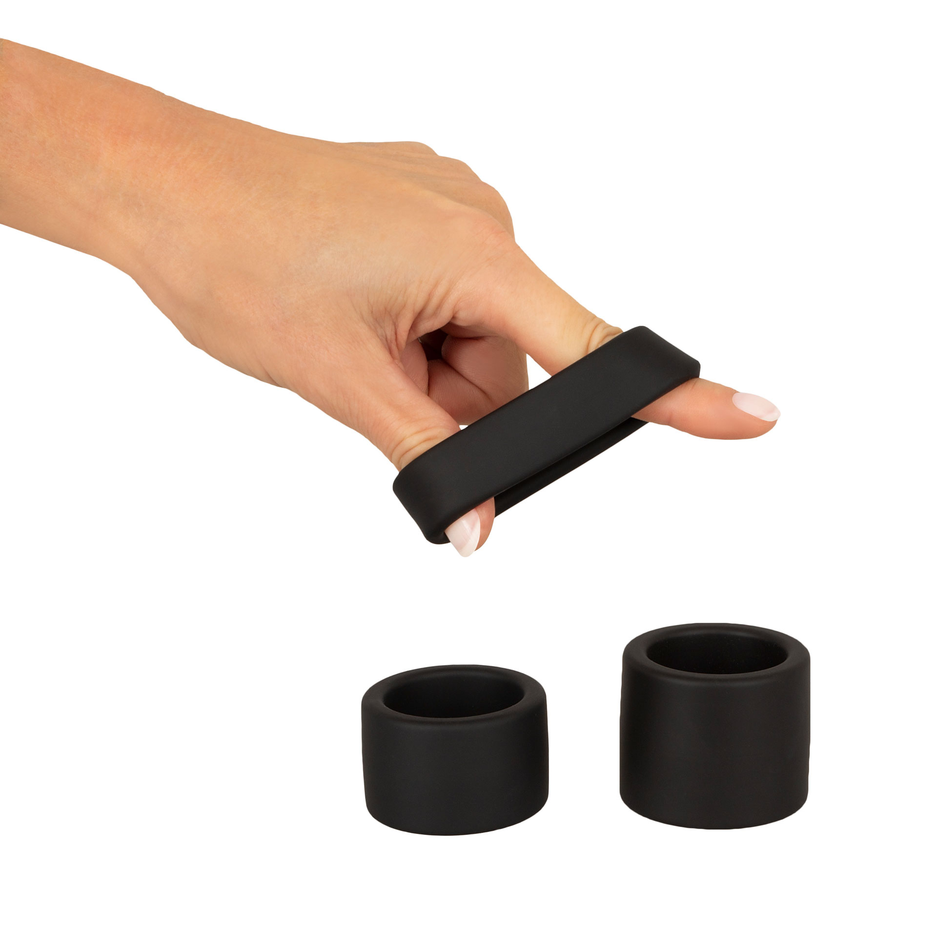 Zwei Finger einer Hand dehnen einen schwarzen Ring. Darunter liegen 2 weitere Ringe.